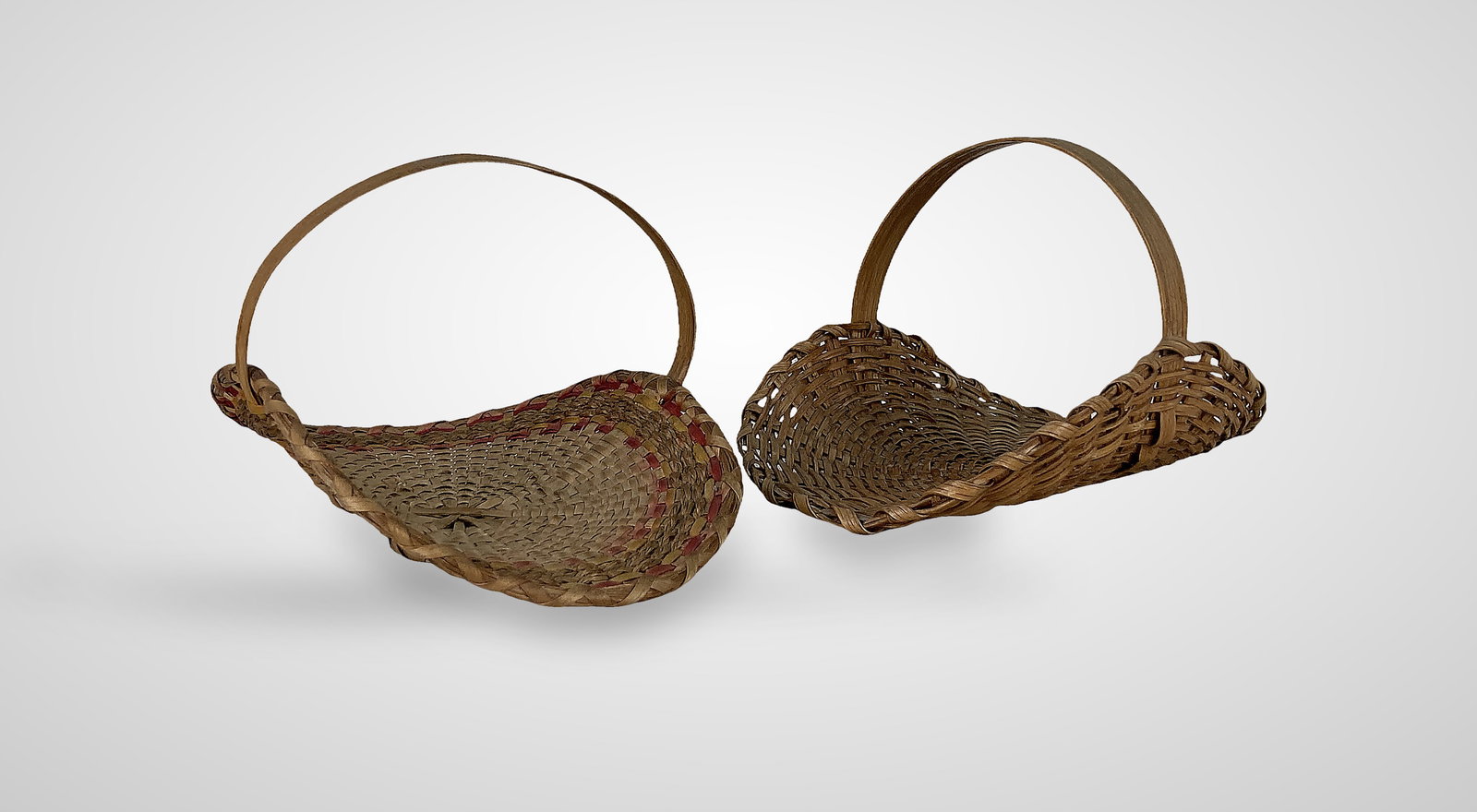 Small Native American Flower Baskets: Two split oak woven flower baskets features a semi-circle shape with a flat edge. One basket is accented with thin, dyed decorative weavers in red and yellow tones and fitted with a bentwood handle, w