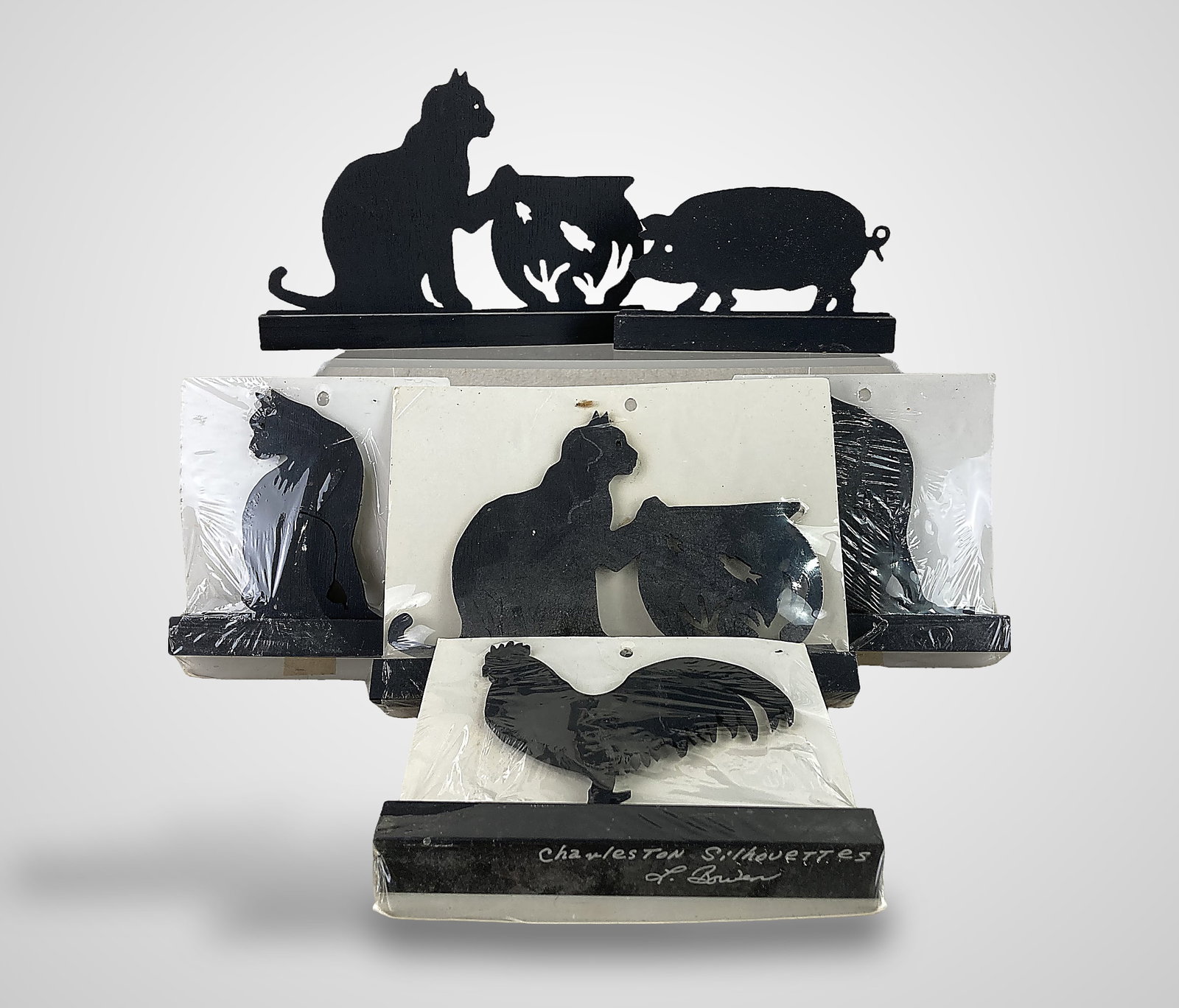Lewis Bowen Carved Animal Silhouettes: Six hand-carved, laminated black wood silhouettes by Lewis Bowen Sr. of Charleston, South Carolina. The assortment features four cat silhouettes, two in a seated pose and two resting a paw on a fishbo
