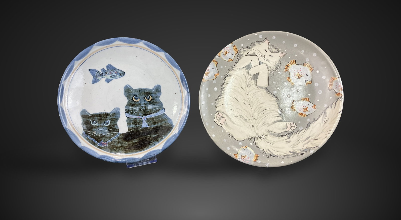 Studio Pottery Cat Plates Featuring Highland Stoneware: Includes two plates featuring charming, hand-painted cat motifs. One plate, by Highland Stoneware of Scotland, depicts two black cats with a fish and a blue border. The second plate, by Mei Ming Ware