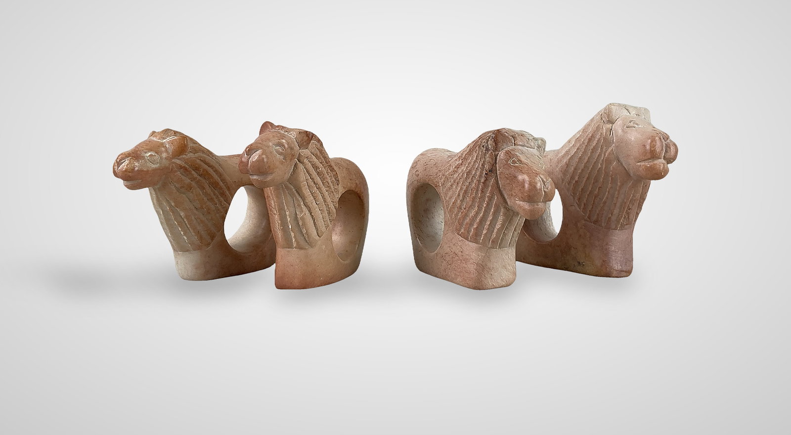 Kenyan Carved Lion Napkin Rings: Four soapstone carved napkin rings in the appearance of male lions. They feature a creamy white and pale pink to rich peach coloration. One measures approximately 2 3/4" H x 1" W x 3 3/8" D. Good