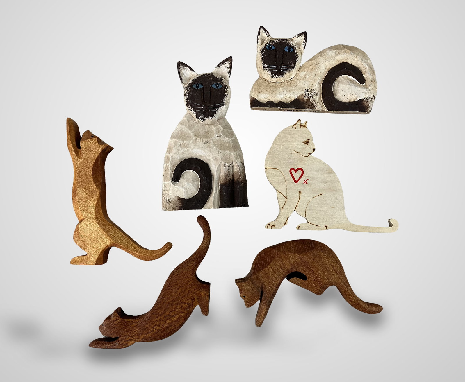 Folk Art Carved Wood Cats: Group of figurines showcases various cat breeds in a wide range of poses, highlighted by two standout Siamese carvings. These Siamese pieces feature expertly applied polychromed details and are