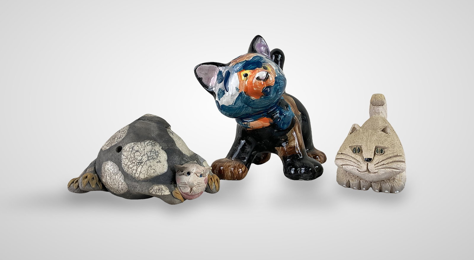 Studio Pottery Cat Figures: Three hand-crafted cat figures are included in this collection. One is a porcelain cat with a hand-painted body in brown, blue, and orange coloration with yellow painted eyes, signed "Jacob" on the bo