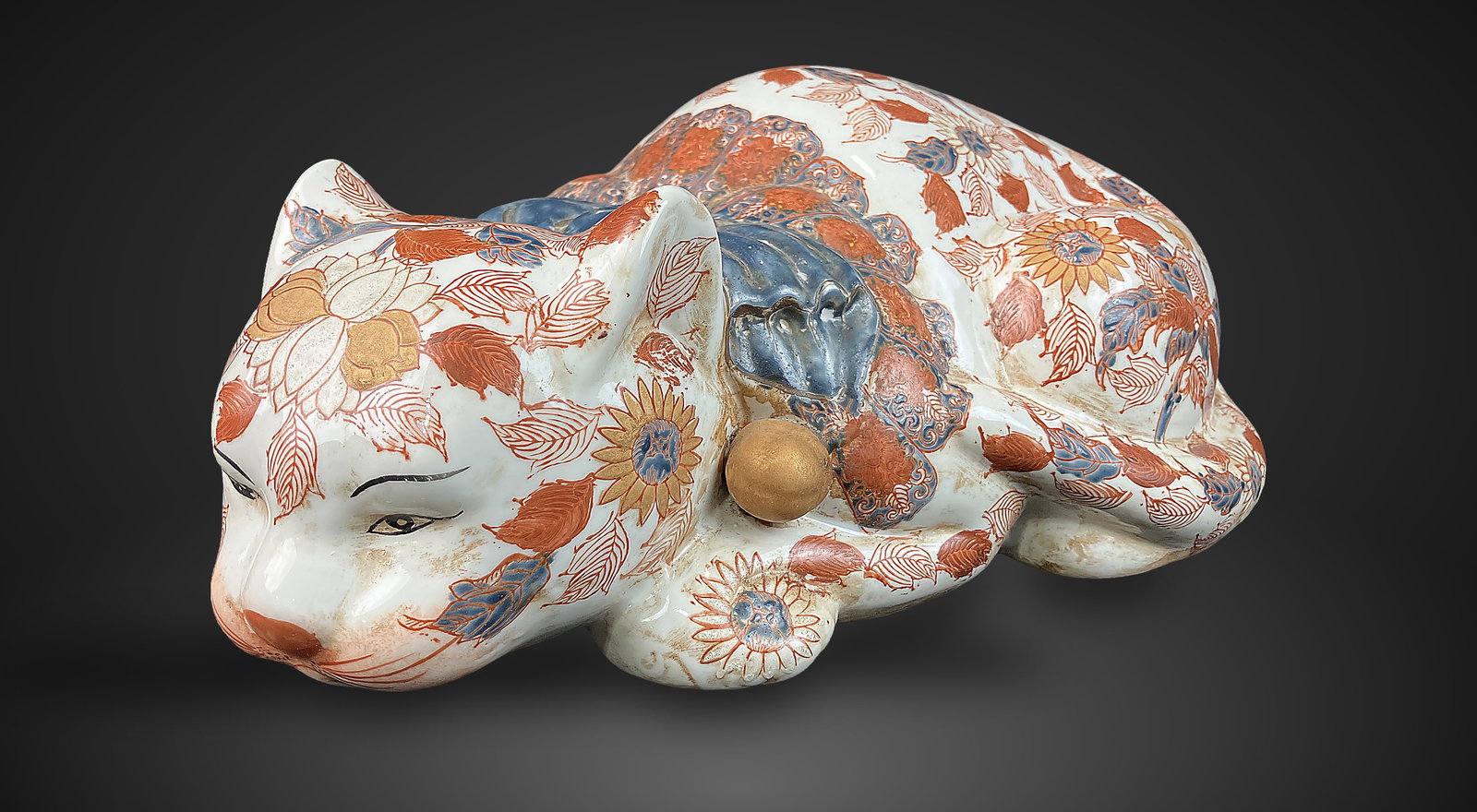 Japanese Imari Sleeping Cat: Medium size porcelain figurine is masterfully decorated with a traditional Japanese Imari palette of red and blue, featuring intricate floral and leafy motifs that define the resting feline form. The