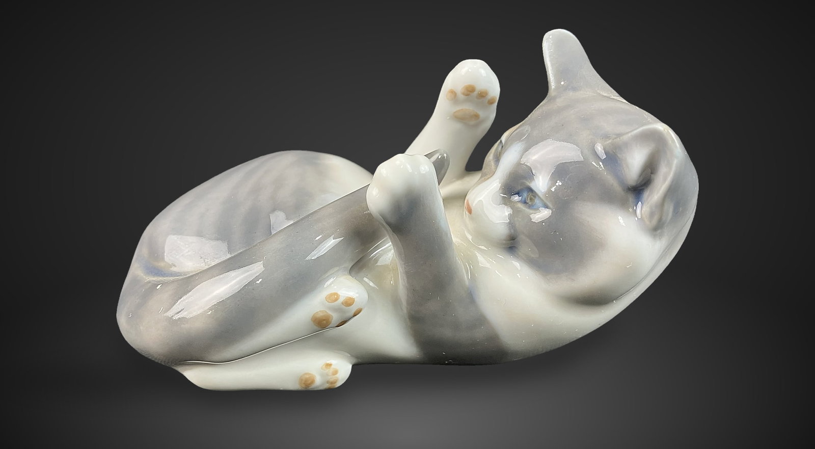 Royal Copenhagen Playful Kitten: This porcelain figurine captures a kitten playfully playing with its tail, showcasing careful artistry with its grey-and-white fur and soft, striking blue eyes. It measures approximately 2 1/4 in. H