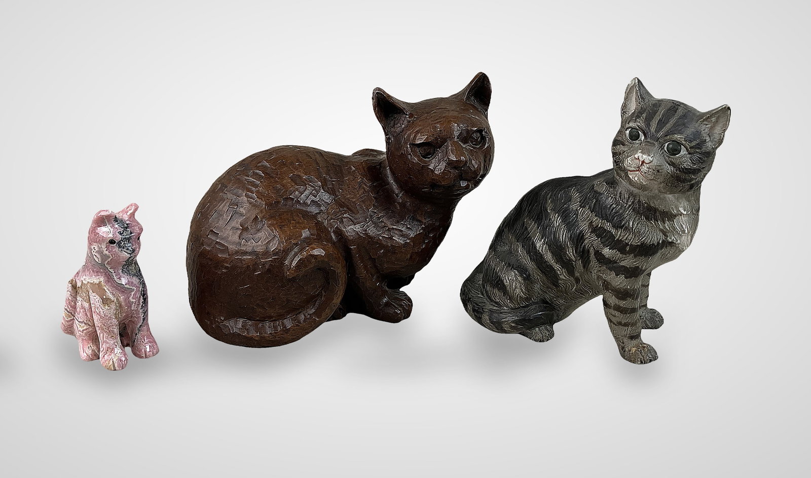 Three Cat Figurines: Diverse collection features three distinct cat sculptures: one small, expertly carved rhodonite figure showcasing rich pink hues; one brown resin piece produced by Red Mill Manufacturing, a maker high