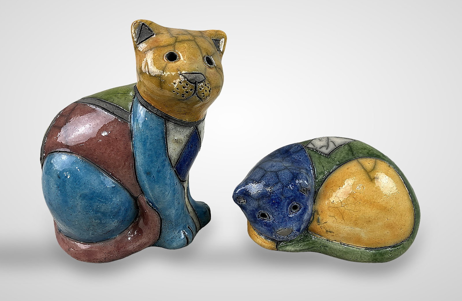 Pair of South African Ceramic Cats: Handmade ceramic figurines showcase distinctive, vibrant, and geometric modern patterning. The set features one seated cat and one in a laying pose, with the tallest measuring approximately 5 1/2 in. 