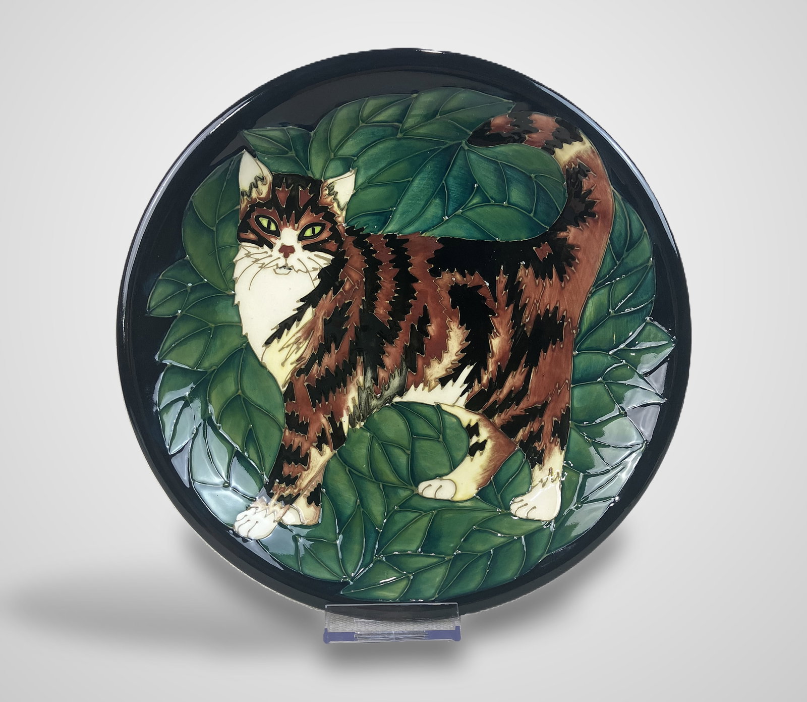 Moorcroft Cat Plate: Designed by Sally Tuffin, this plate features a tube-lined ginger and black tabby cat with white accents against a leafy background and is signed "WM" on the reverse for English maker Walter