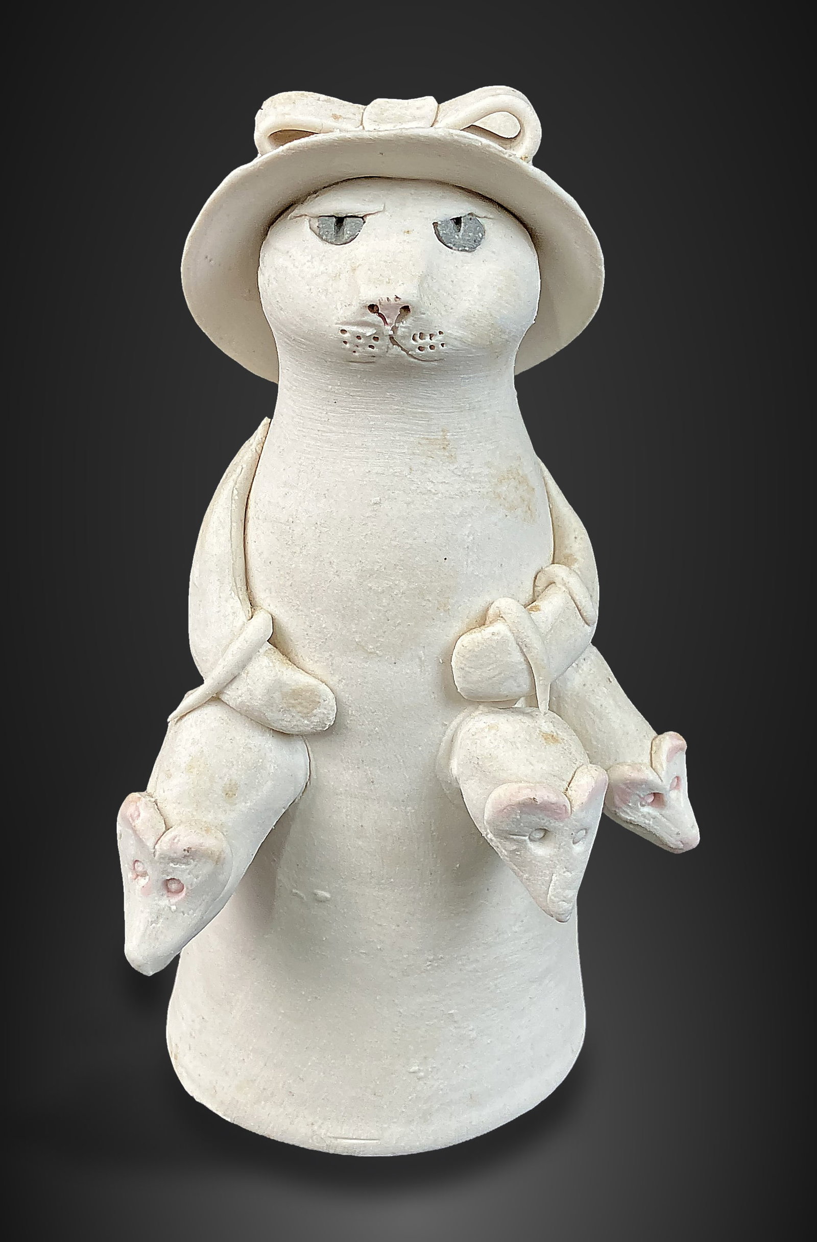 Solveig Cox Cat Pottery Figurine: Charming sculptural piece depicts a cat wearing a sunhat and holding mice, finished in a bisque glaze. It is signed on the reverse. Created by the prominent American studio ceramic artist and
