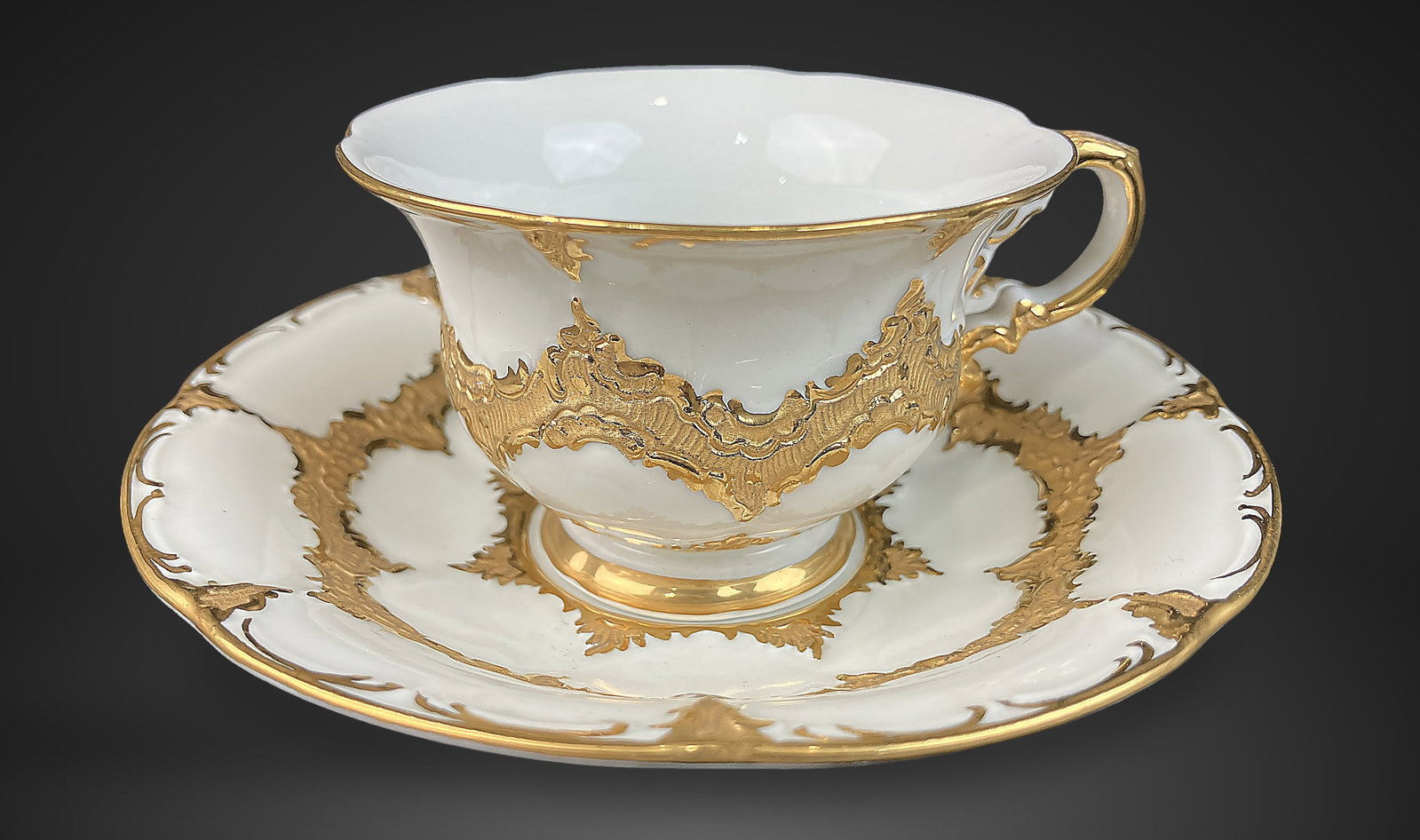 Gilt Decorated Meissen Cup and Saucer: Delicate demitasse set features dramatic embossed gold decoration in a Rococo style, beautifully contrasted against a crisp white porcelain form. The saucer measures approximately 1 in. H x 4 7/8 in.