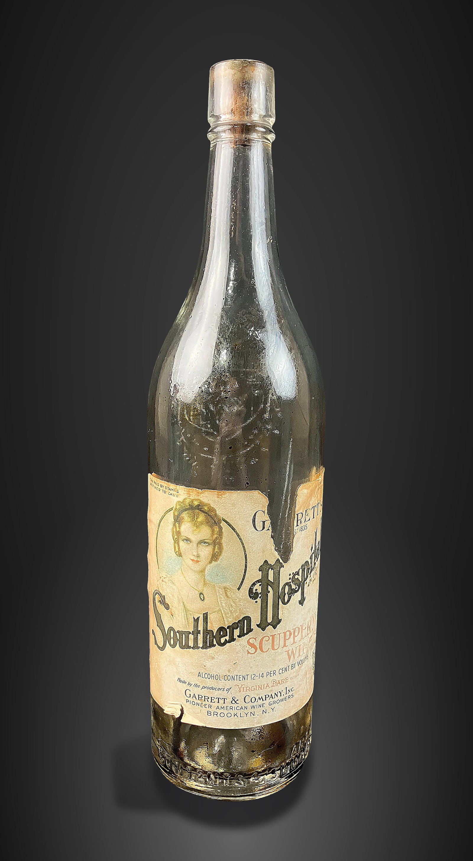 1920s Garrettâ€™s Southern Hospitality Bottle: Alcohol bottle from Garrett and Company of Brooklyn, NY, captures the essence of the 1920s with a printed label featuring an Art Deco woman sporting a classic flapper hairstyle and dramatic makeup.