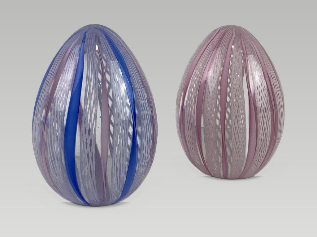 Murano Glass Egg Paperweights: This set of two egg-shaped paperweights is by Murano. Both pieces display the laticinio technique; one features vertical ribbons in blue, pink, and white, while the other is decorated with pink and