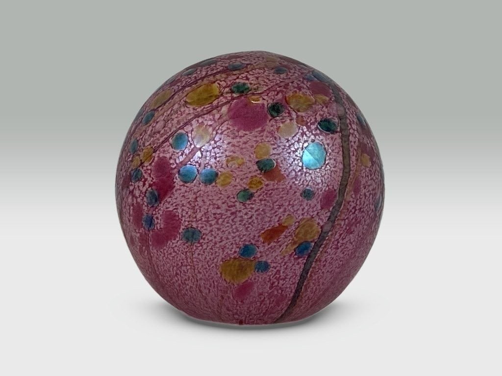 Isle of Wight Summer Fruits Art Glass Paperweight: This cranberry glass spherical paperweight is an authentic Isle of Wight piece featuring a distinctive pink speckled surface accented with small colored spots. It measures approximately 2 3/8 in. H x