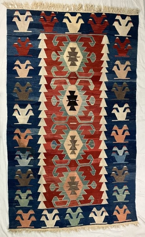 Turkish Kilim Rug: This hand-woven Turkish kilim rug is crafted from natural wool using traditionally used dyes, featuring geometric patterning and vegetal symbolic motifs in rich blues, reds, and other tones.