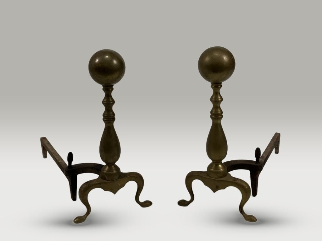 Pair of Brass Andirons: Pair of brass andirons features classic baluster forms topped with large cannonball-style finials. Measuring approximately 17 in. H x 8 in. W x 18 3/4 in. D, the pieces display natural wear accompanie
