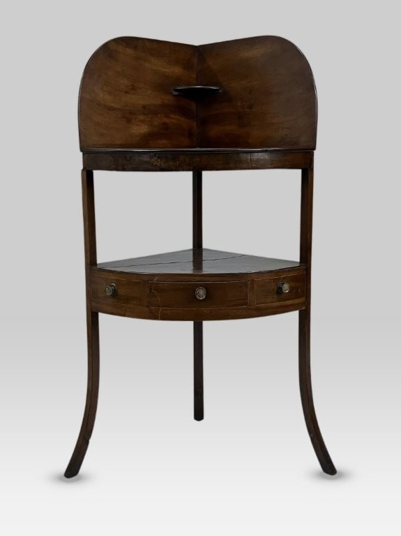 Georgian Corner Washstand: 19th-century George III bow-front corner washstand is crafted from rich walnut wood with a deep patina and features a shaped back, tapered and flared legs, hand-cut dovetails, and a single drawer