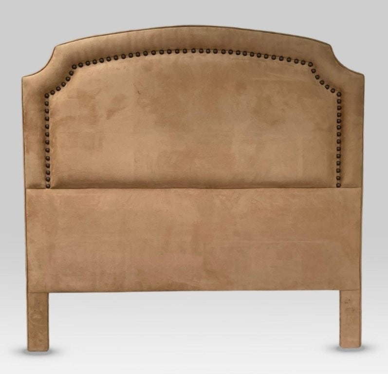 Suede Embellished Queen Size Headboard: A queen size upholstered headboard in a neutral suede, the shaped form defined by decorative nail head trim accents; 59 in. H, 61 in. W, 2 5/8 in. D. Some surface wear.