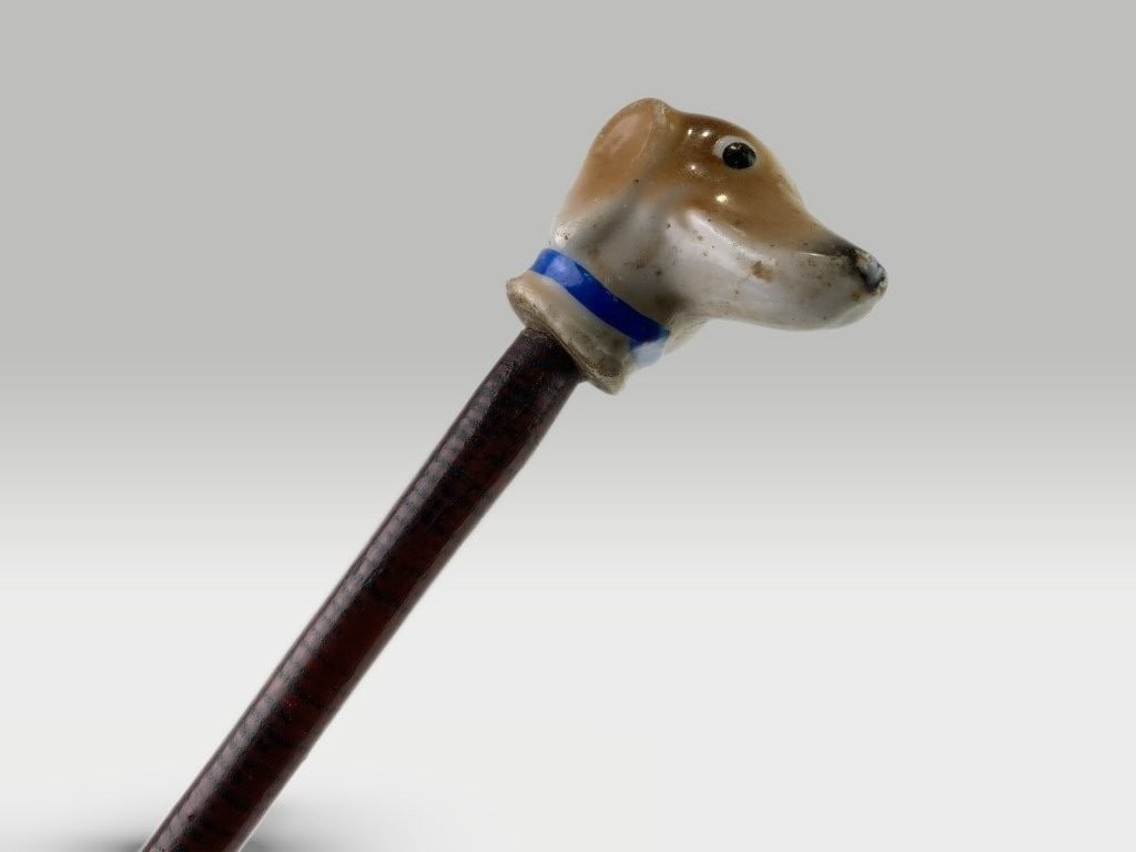 Polychromed Carnival Dog Cane: Folk art cane features a carved hunting dog head as the handle, crafted from pine with a polychromed simulated wood finish. It measures approximately 33 3/4 in. H x 1 1/4 in. W x 1 7/8 in. D and