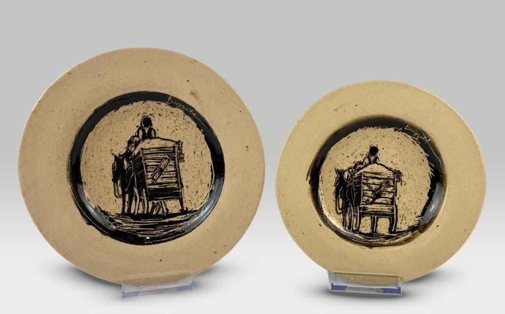 Donnie Baggett Folk Art Pottery Plates: Two folk art plates by Mississippi artist Donnie Baggett—who operated out of the Raymond Train Depot during the 1970s—feature traditional Southern scenes of a man driving a donkey cart.