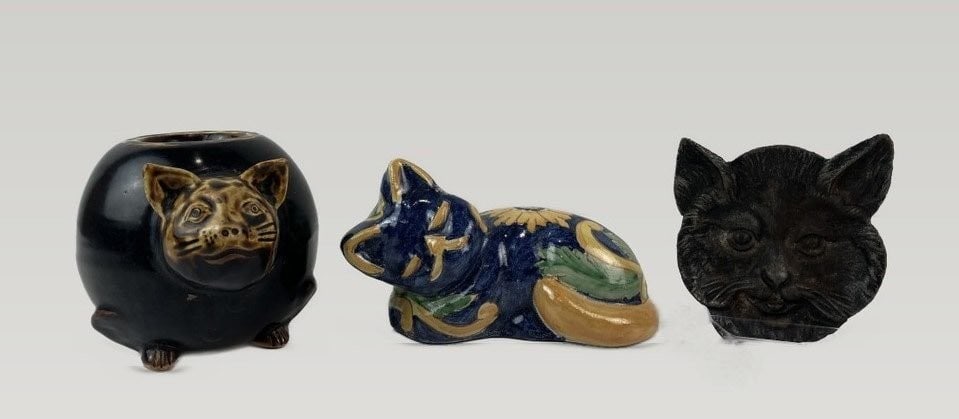 Assortment of Cat Figurines: Assortment of cat-themed decorative items includes three pieces: an Italian glazed earthenware figurine decorated with flower and leaf designs in tones of yellow, blue, and green; a cast iron cat face