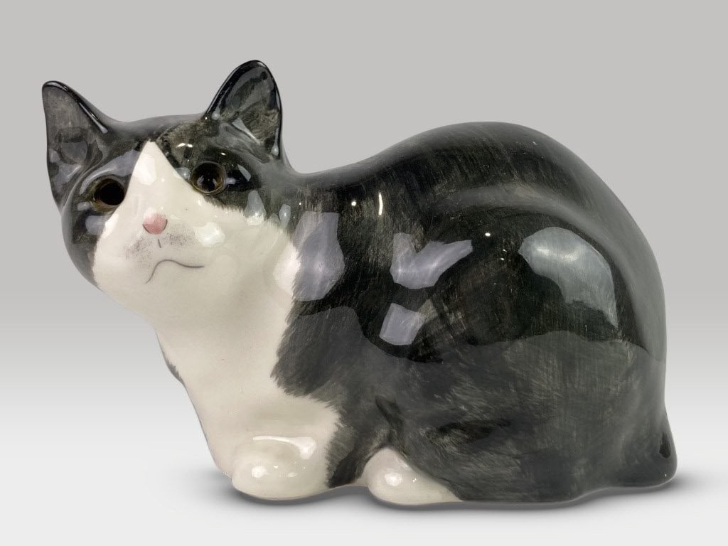 Ceramic Cat Figurine: This ceramic figurine depicts a gray and white cat seated in a relaxed pose with charming, detailed features. It measures approximately 7 in. H x 4 in. W x 9 1/4 in. D. The piece exhibits a loss to on