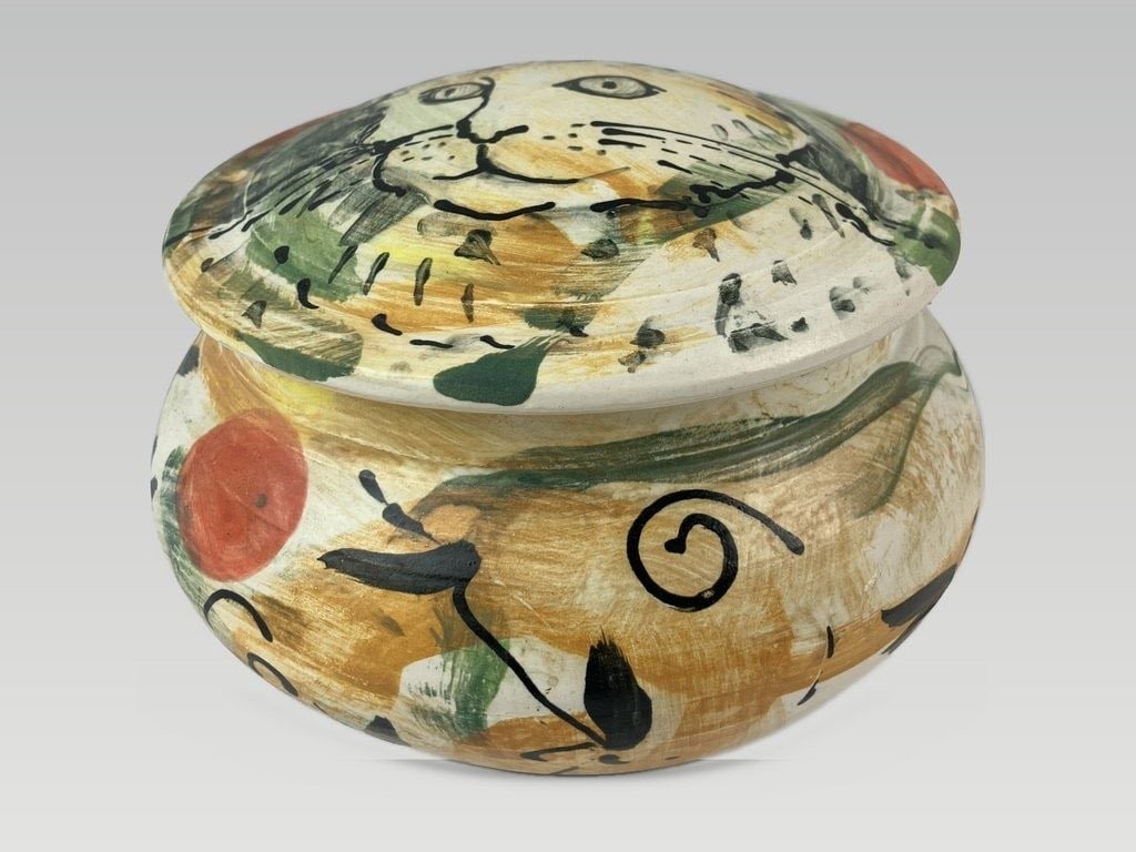 Studio Pottery Cat Covered Dish: This covered vessel features a hand-painted cat design on the lid set against a slip glaze, complemented by vibrant abstract painting along the sides. The interior is finished in a striking, vibrant b