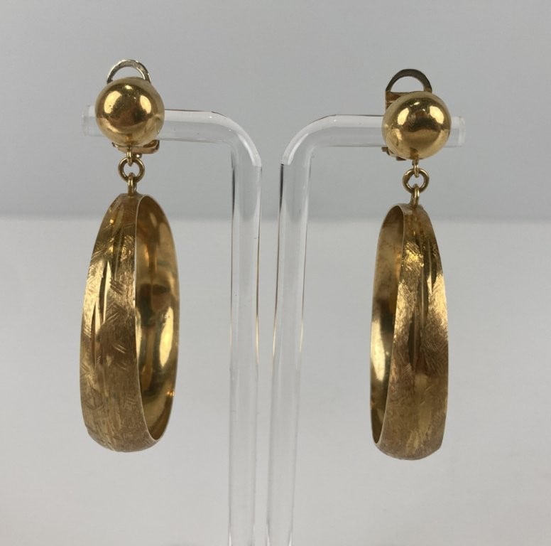 18KT Gold Dangle Hoop Earrings: These hoop earrings are crafted in 18-karat yellow gold, marked and verified by testing. Each large hoop features intricate, fine engraved detailing across the gold surface and is secured with