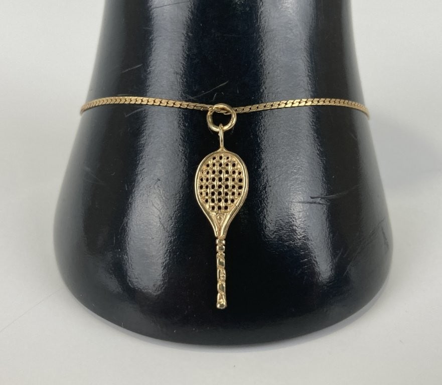 14KT Gold Tennis Motif Charm Bracelet: Delightful fine jewelry bracelet features a streamlined yellow gold chain accented by a charming dangling tennis racket pendant. Both the tennis racket charm and the secure clasp are marked for gold