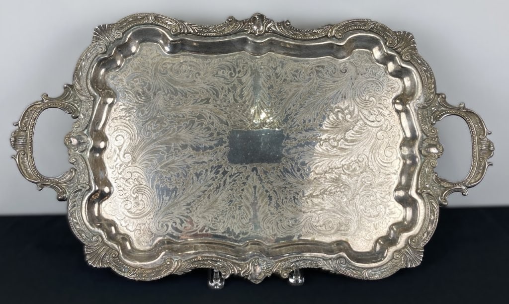 Silverplate Serving Tray: Elegant silver-plated footed serving tray features an ornate scrollwork edge accented with delicate beading and integrated handles, complemented by finely decorated leafy botanical motifs across the