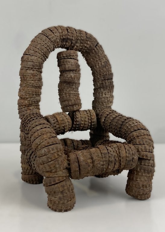 Folk Art Bottle Cap Chair: This unique folk art rustic chair sculpture is meticulously crafted from stacked, weathered metal bottle caps. Featuring curved armrests and an arched back support, the piece displays a worn aged