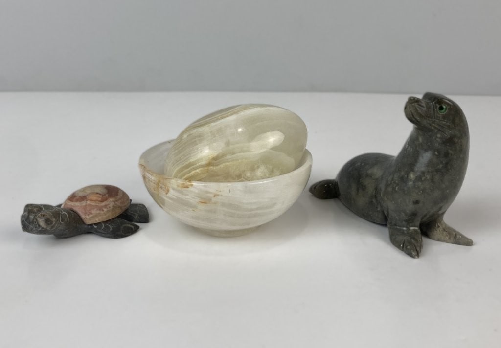 Stone Decorative Assortment: The grouping includes a smooth light onyx egg and a matching bowl, a whimsical carved turtle adorned with a vibrant polished agate stone, and a sleek grey polished stone seal. The onyx egg measures