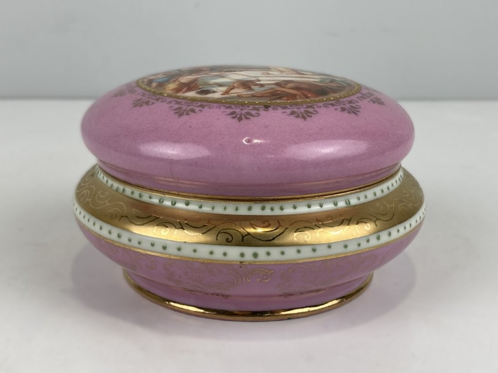 Epiag Porcelain Trinket Box: This round Czechoslovakian porcelain trinket box depicts a classical mythological scene of men conversing within a courtyard on the lid, complemented by a hand-painted interior design featuring two