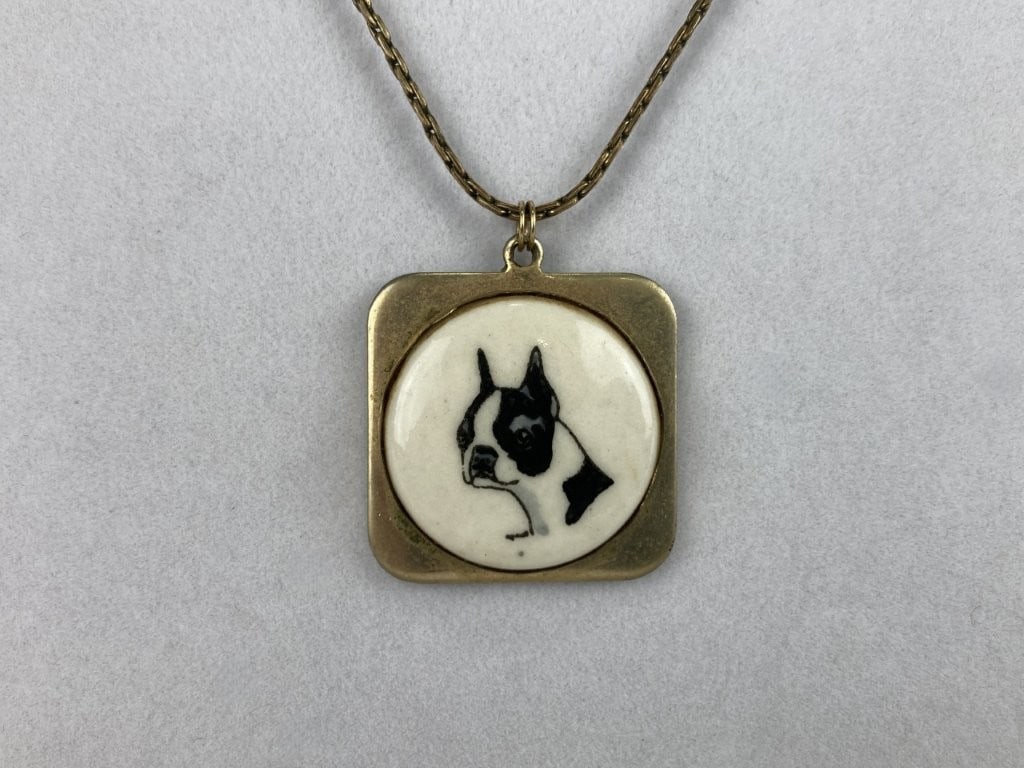 Porcelain Boston Terrier Pendant Necklace: This charming vintage necklace features a central porcelain medallion hand-painted with a detailed depiction of a Boston Terrier, surrounded by a classic gold-tone square frame. The pendant is
