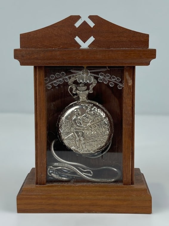 Hunting Motif Pocket Watch and Display: Timepiece features a brilliant silvertone pocket watch decorated with an intricate figural hunting motif on the exterior case, accompanied by a matching watch fob measuring approximately 14 in. in