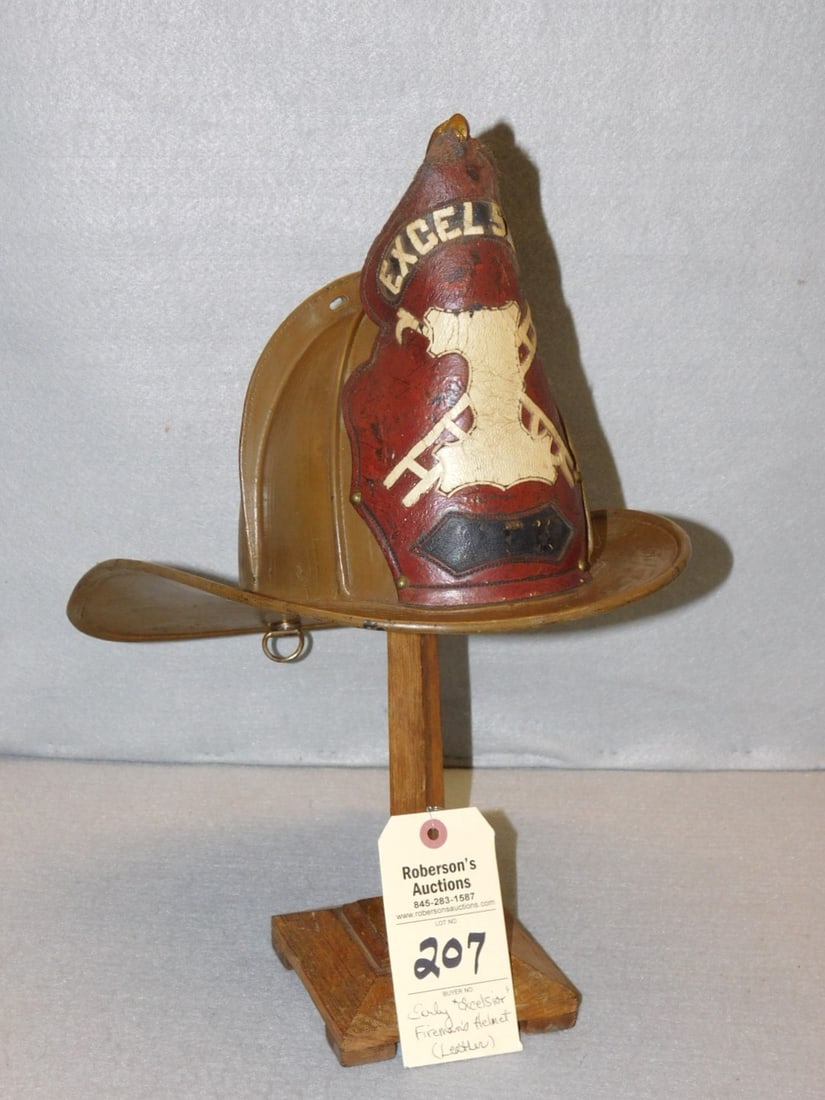 Early "Excelsior" Fireman's Helmet: Early "Excelsior" Fireman's Helmet, Made of Leather w/Shield w/Ladder & Fire Hook(i is missing on name), Otherwise gd. cond. 9"H x 15L x 10-3/4"W