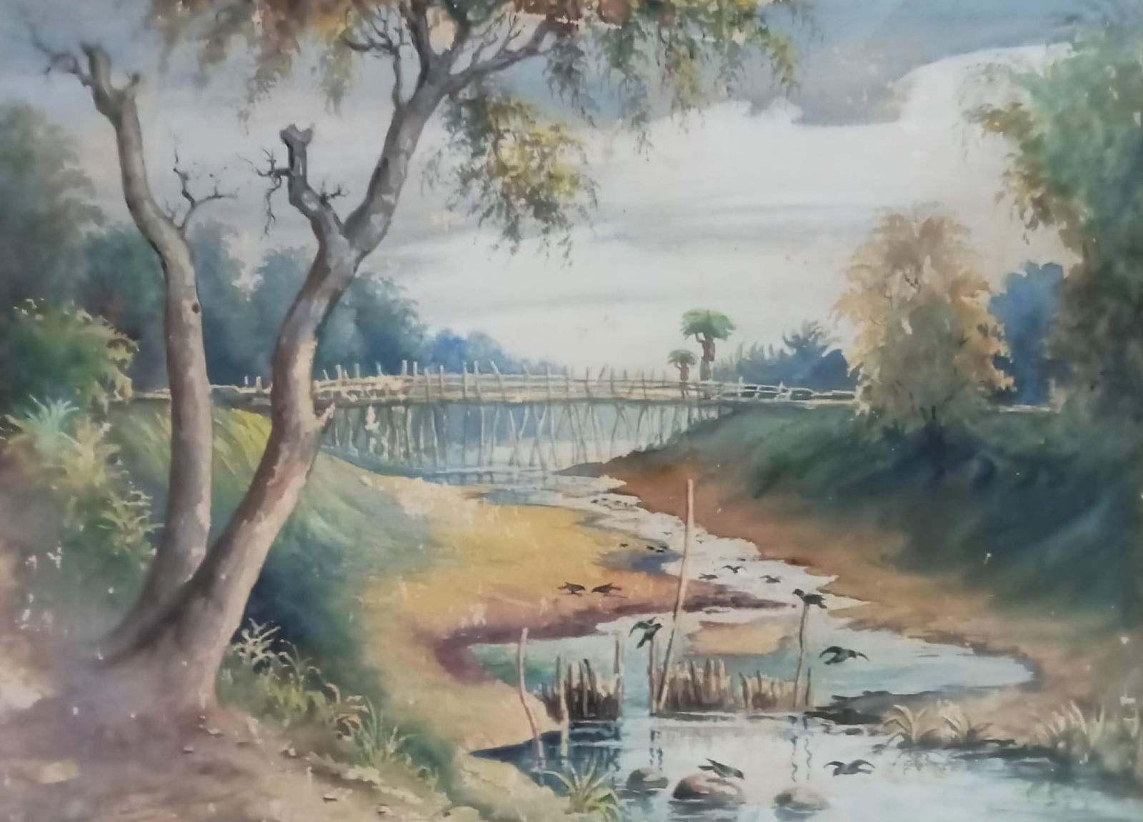 J. P. GANGOOLY (INDIAN, 20TH CENTURY) l WATERCOLOR ON PAPER l RIVERSIDE LANDSCAPE WITH WOODEN BRIDGE: P. GANGOOLY (INDIAN, 20TH CENTURY) l WATERCOLOR ON PAPER l RIVERSIDE LANDSCAPE WITH WOODEN BRIDGE l SIGNED LOWER RIGHT, 22 X 16 IN. J. P. GANGOOLY’S TRANQUIL WATERCOLOR COMPOSITIONS ARE CELEBRATED