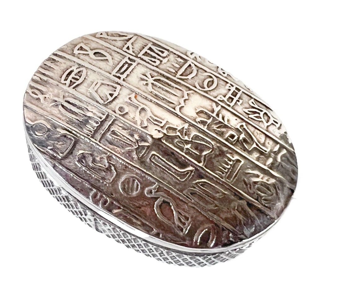 Egyptian 840 silver Pill Box with hieroglyphics c1920: Egyptian 840 silver Pill Box with hieroglyphics, c1920. Raised hieroglyphic designs on lid, cross hatch texture on side. Hallmark on bottom. Measurements: Approx. 17.85grams. 1.125 x 1.625 x 0.5 inche