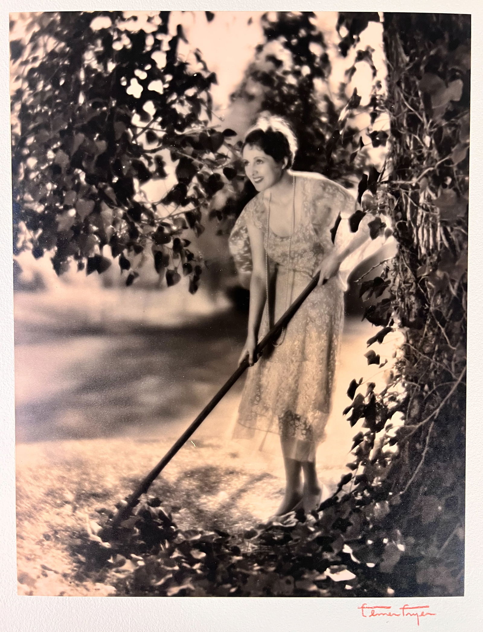 Elmer Fryer Sepia Tone photograph of Billie Dove c1930: Elmer Fryer (American 1898-1944) Sepia Tone silver gelatin photograph, Silent film actress Billie Dove, raking leaves; signed lower right on board the photo is mounted to. (D2)print 13.375 x 10.375; b