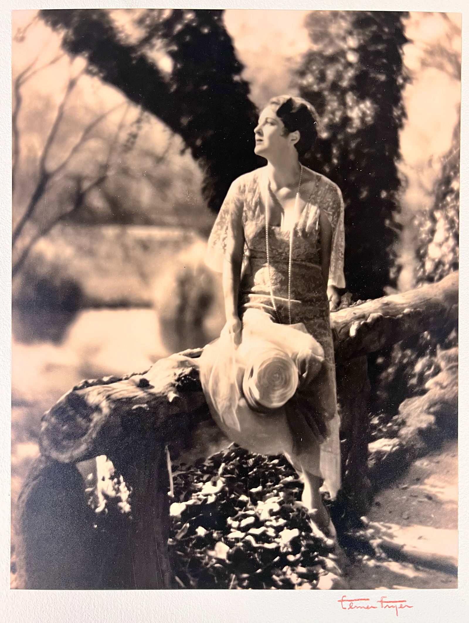 Elmer Fryer Sepia Tone photograph of Billie Dove c1930: Elmer Fryer (American 1898-1944) Sepia Tone silver gelatin photograph, Film actress Billie Dove, seated on a log; signed lower right on board the photo is mounted to. (D2) Measures Approx., print 13.3