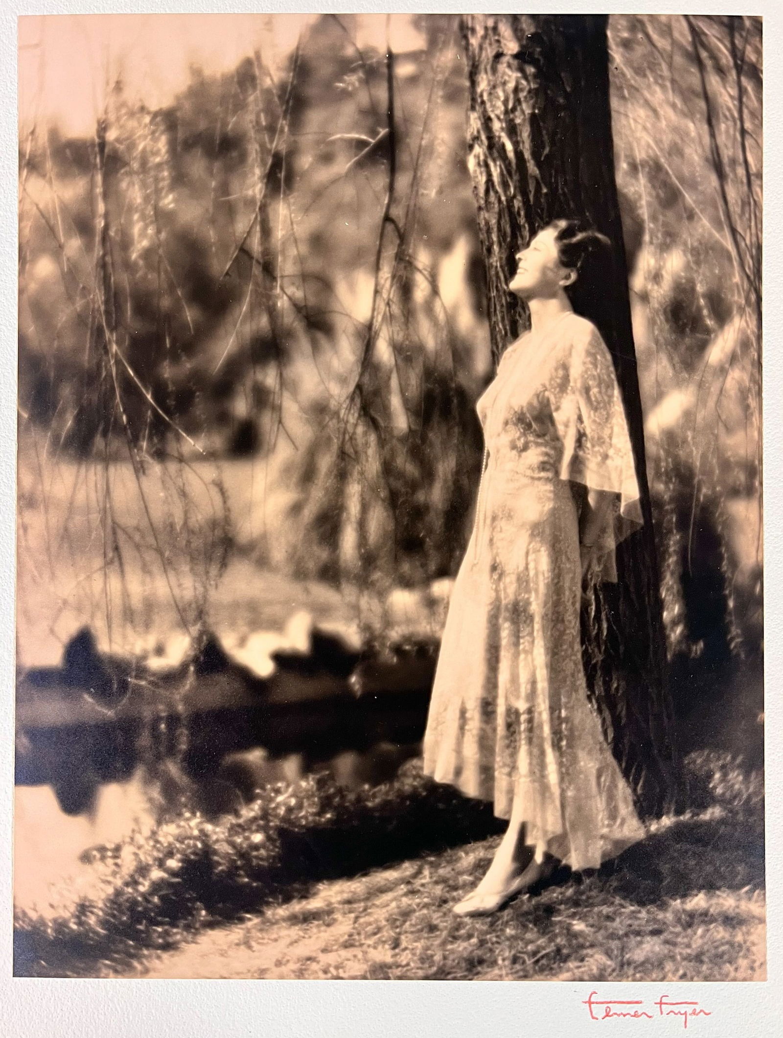 Elmer Fryer Sepia Tone photograph of Billie Dove c1930: Elmer Fryer (American 1898-1944) Sepia Tone silver gelatin photograph, Film actress Billie Dove, leaning against a tree by a stream; signed lower right on board the photo is mounted to. (D2) Measureme