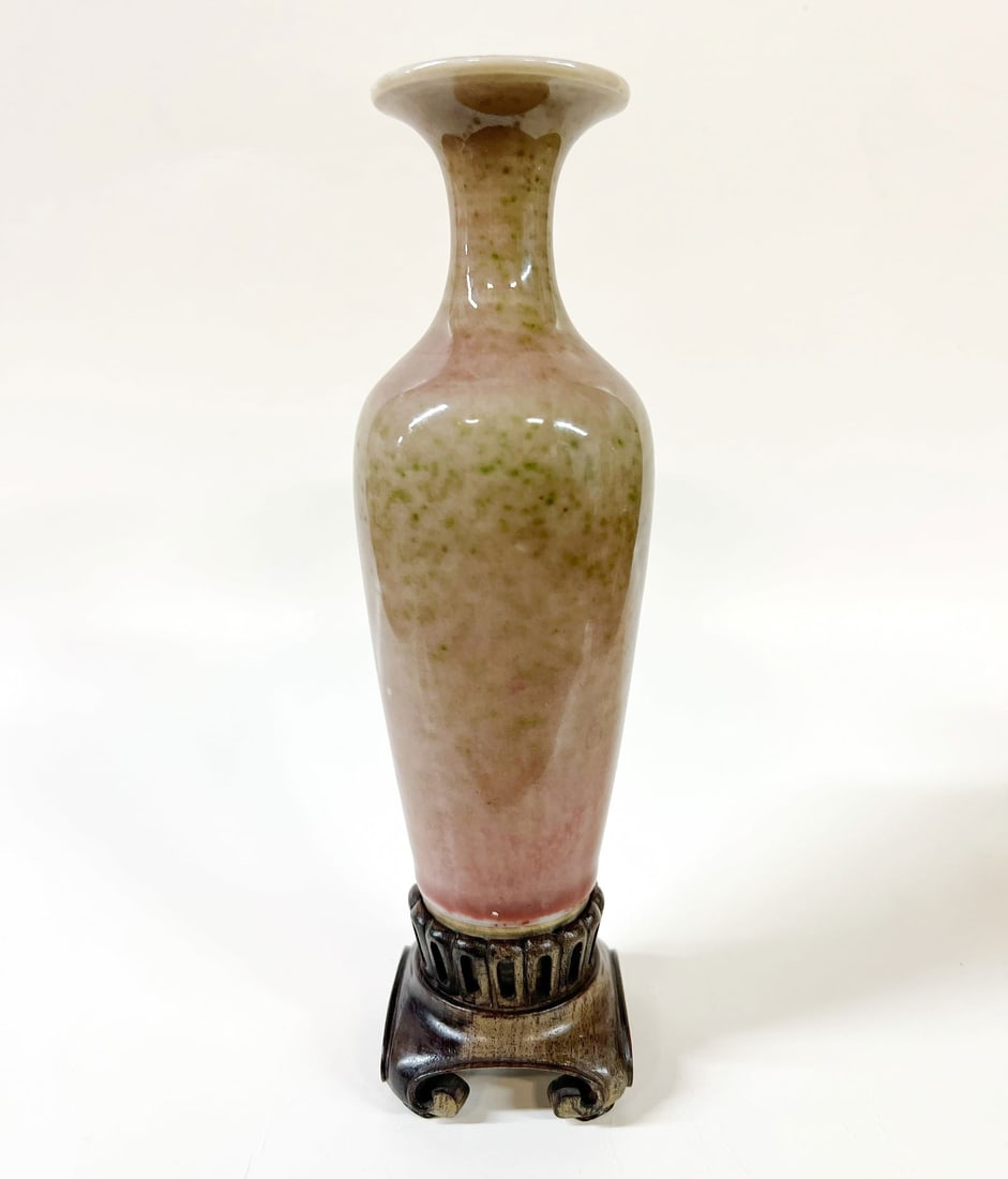 Chinese Peach Bloom glazed Liuyeping Vase: Small peach bloom glazed amphora-shaped or willow leaf vase on carved wood stand. Flared mouth, mottled colors from a pink to green. Unmarked. 7.25 in height with stand; 6.375 x 2 inches w/out stand D