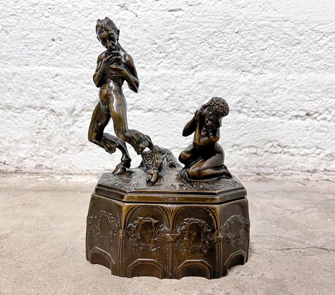 Max Drah 1879-unknown Patinated Bronze Box Figural Lid Nude and Satyr: Max Drah (1879 -?) Patinated Box Nude and Satyr Bronze. A pan or satyr plays the lute, a nude woman kneels behind him. Marked 'DRAH'. Interior lined with fabric. 6.5lb Measurements: Approx. 10 inches