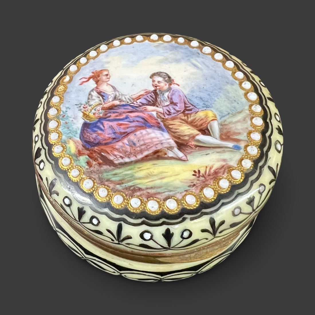 Continental Gilt Bronze Hand Painted Jeweled Porcelain Snuff Trinket Box c1880: Continental Gilt Hand Painted Jeweled Porcelain Snuff Box c1880; featuring a idyllic courting couple, raised enamel 'jewels', vine motif. Gilt bronze/metal. Unmarked. Measurements: Approx. 2 inches di