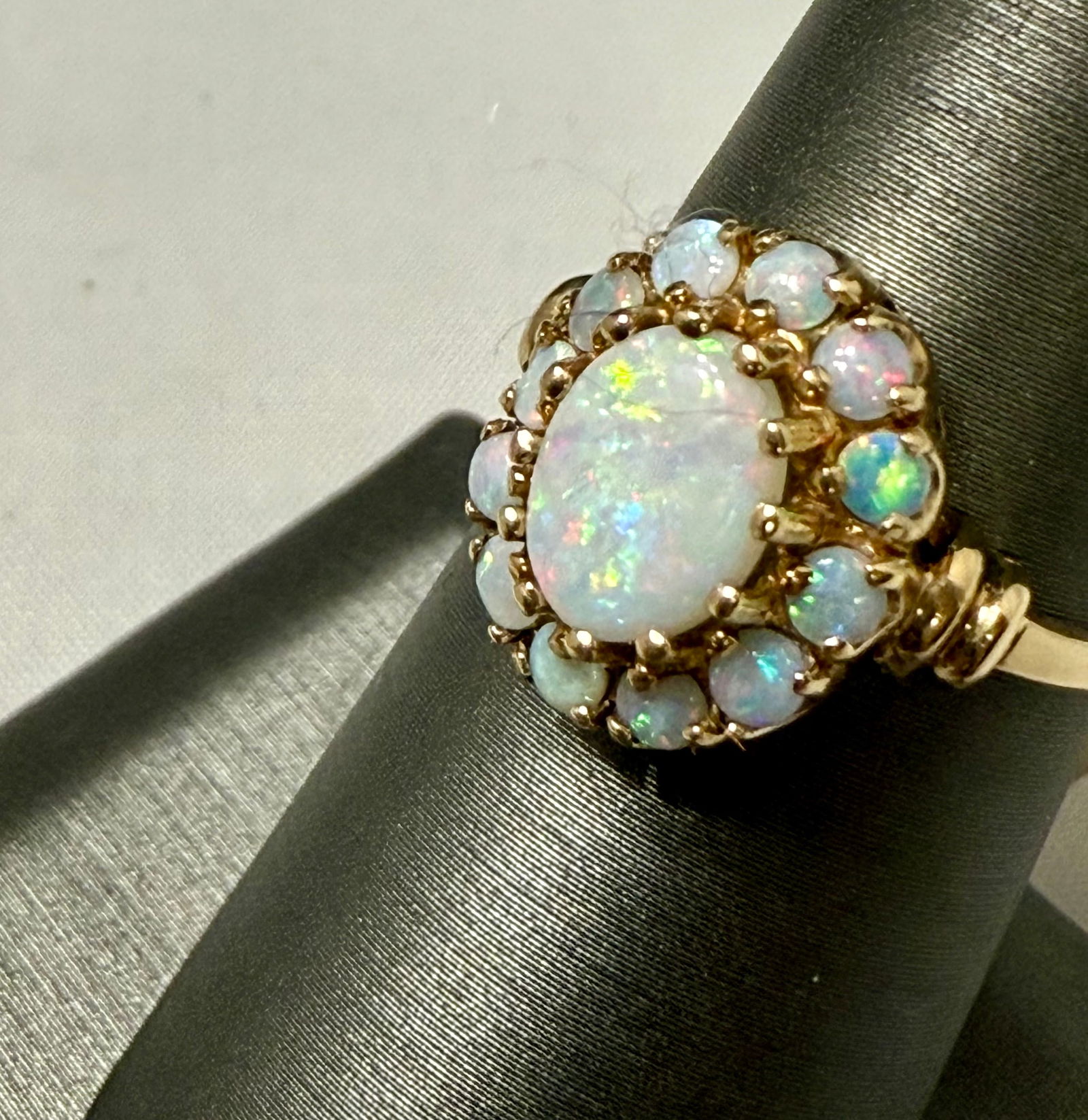 Opal Cluster Ring, in 14K Yellow Gold Size 6 3/4: Glowing with the colors of the northern lights, this vintage 14K yellow gold ring features a luminous oval opal at its center, surrounded by a radiant halo of smaller opals—each alive with shifting