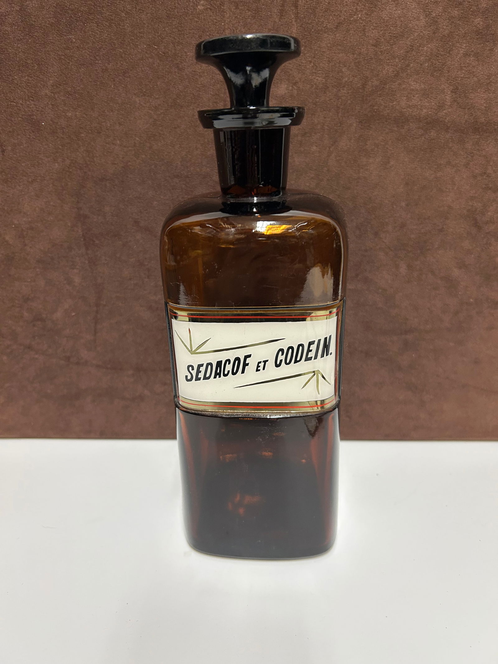 Amber Glass Apothecary Bottle Labeled “SEDACOF ET CODEIN.”: This antique amber glass apothecary bottle, measuring approximately 10 inches tall by 3 inches wide, dates to the late 19th or early 20th century. It would have once contained a medicinal preparation