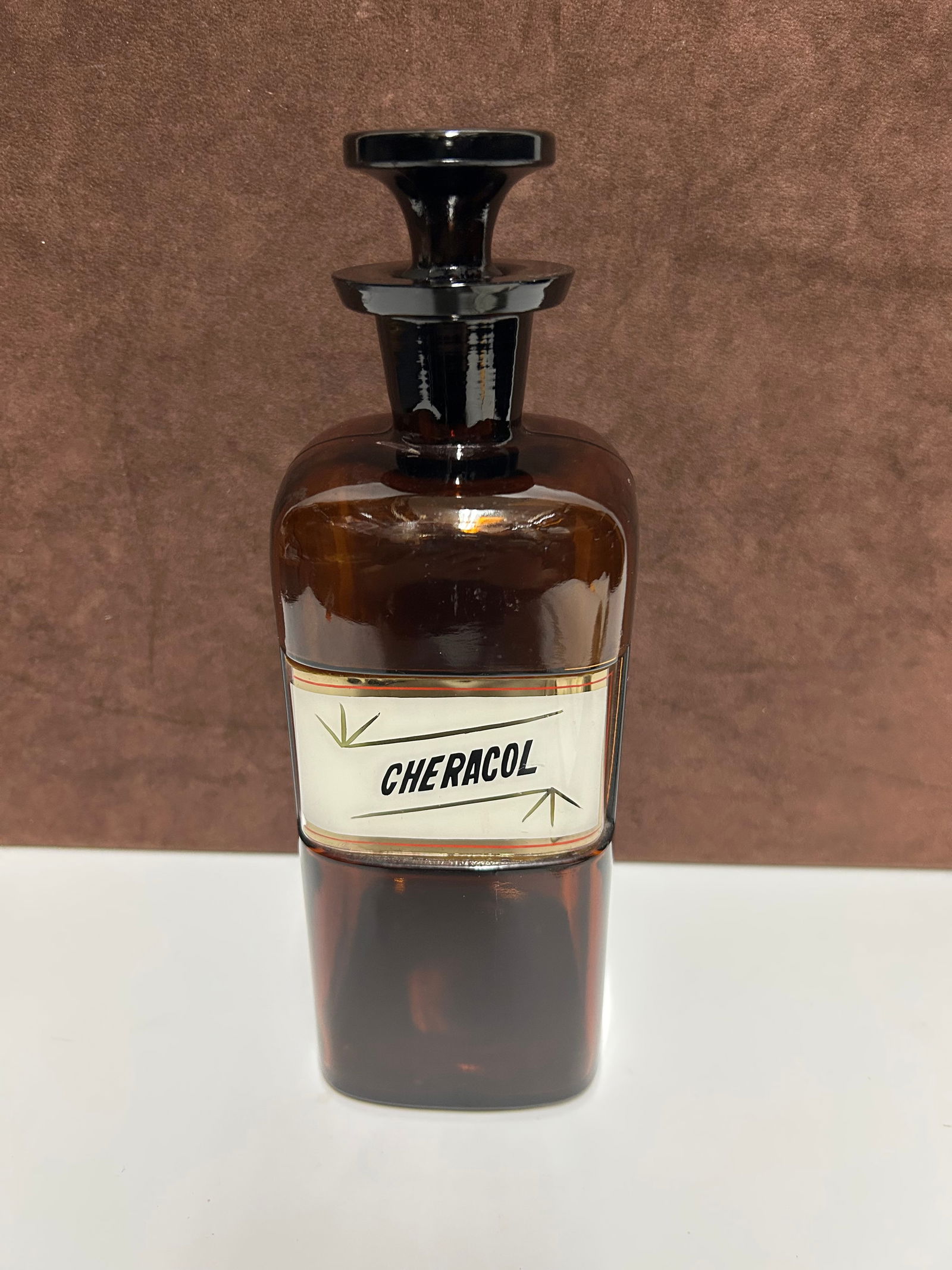 Amber Glass Apothecary Bottle Labeled “CHERACOL”: This antique amber glass apothecary bottle, measuring approximately 10 inches tall by 3 inches wide, dates to the late 19th to early 20th century. It originally held Cheracol, a pharmaceutical cough p