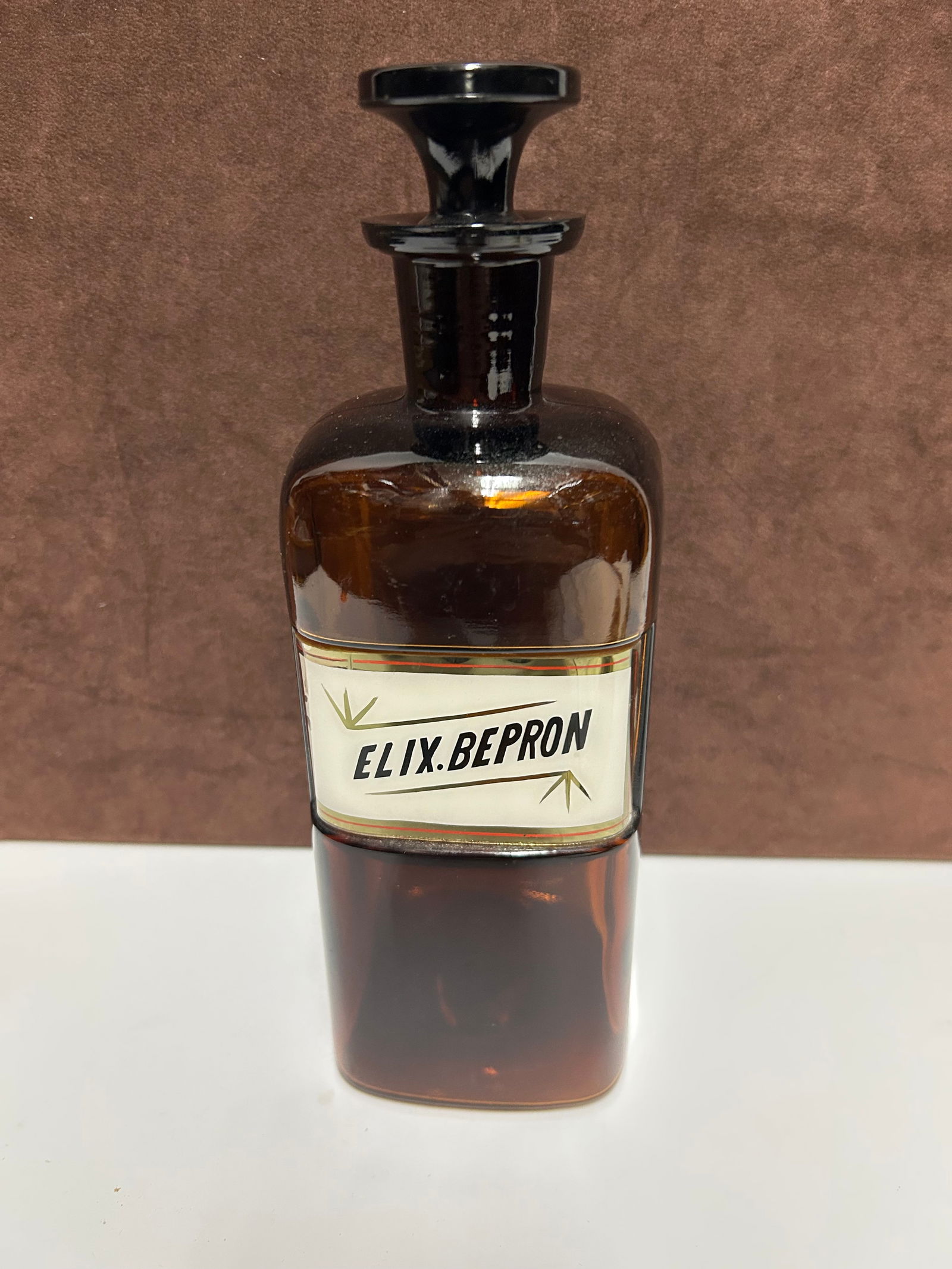 Amber Glass Apothecary Bottle Labeled “ELIX. BEPRON”: This antique amber glass apothecary bottle measures 10 inches tall by 3 inches wide and dates to the late 19th century, likely between 1850–1900. Designed for professional pharmacy use, it features