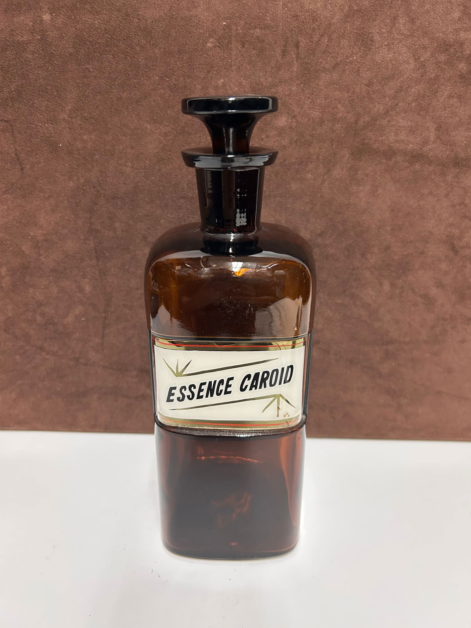 Amber Glass Apothecary Bottle Labeled “ESSENCE CAROID”: This antique amber glass apothecary bottle measures 10 inches tall by 3 inches wide and dates to the late 19th to early 20th century, during a period when pharmacists dispensed medicinal preparations