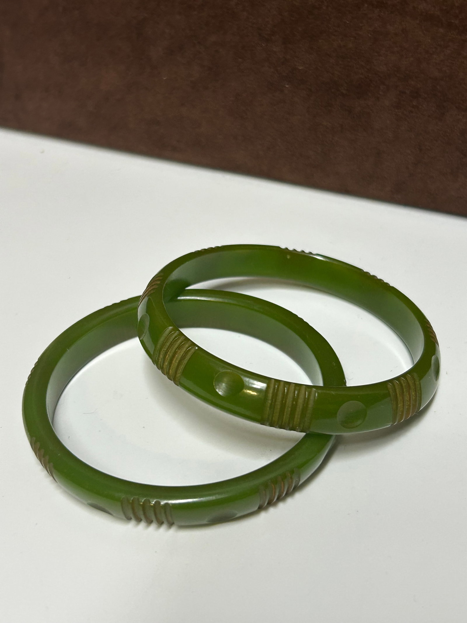 Vintage Pair of Carved Green Bakelite Bangle Bracelets: This is a lovely matched pair of vintage carved Bakelite bangle bracelets in a rich jade-green tone. Each bracelet features hand-carved linear ribbing and circular dot accents, showcasing the classic 