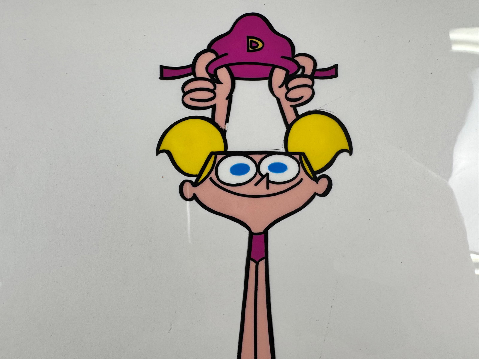 Dexter’s Laboratory Original Animation Production Cel Dexter Hand Painted Transparent: This original animation production cel depicts Dexter holding a hat with the letter D above his head. The cel includes a signature in the lower right corner.