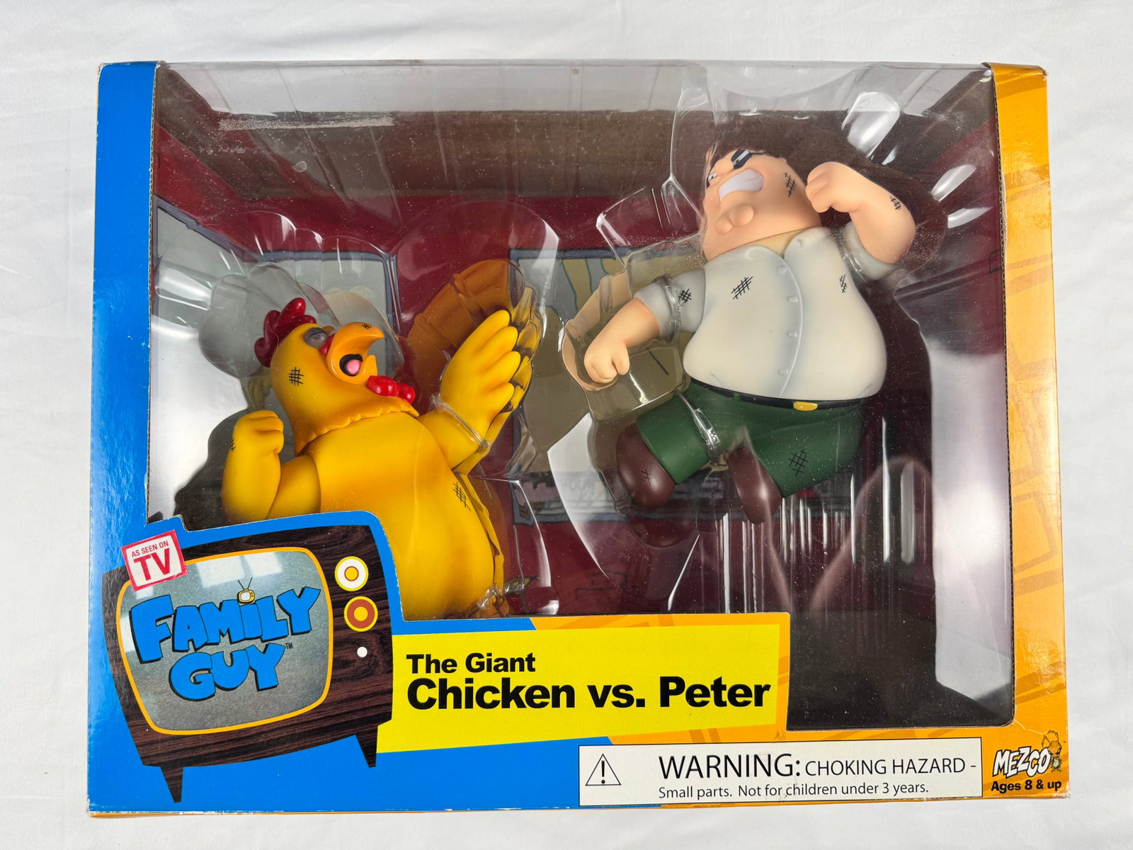 Family Guy The Giant Chicken vs Peter Mezco Boxed Figure Set: This boxed figure set depicts The Giant Chicken vs. Peter from the television series Family Guy. The packaging includes Mezco branding and product labeling.